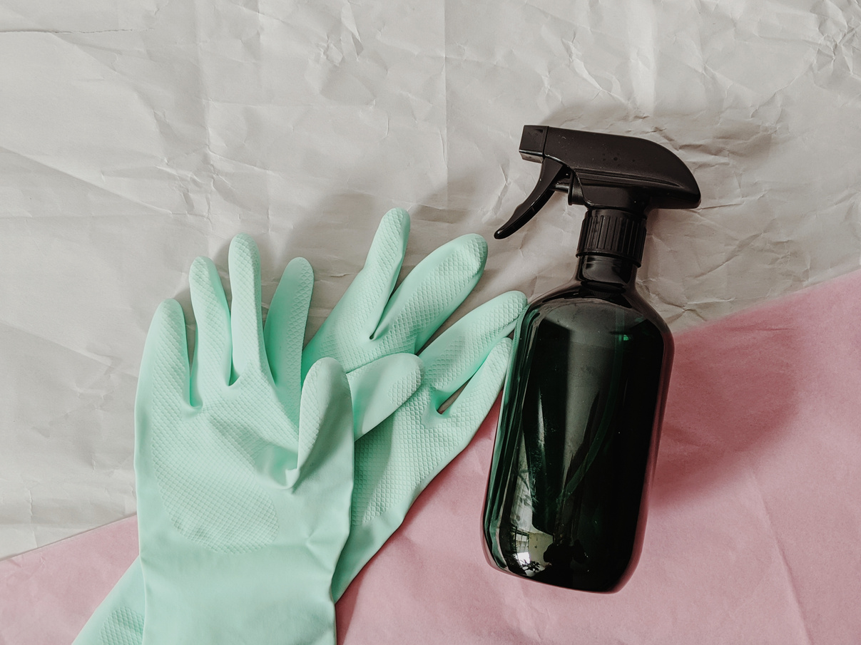 Rubber gloves and a spray bottle on pink and white background